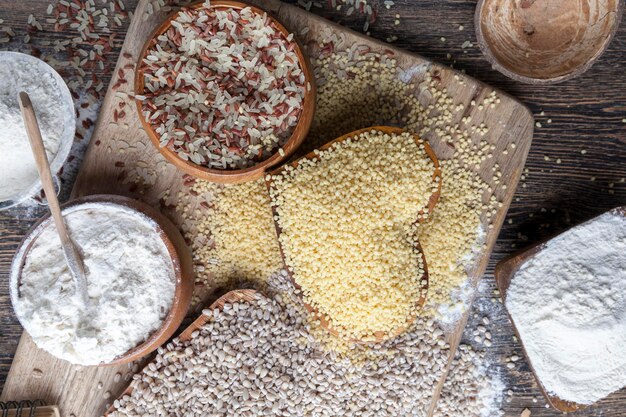 A close-up shot of various gluten-free grains and flours, such as quinoa, rice, almond flour, and tapioca starch, arranged in small bowls on a wooden table. A measuring spoon is next to one of the bowls, emphasizing the importance of accurate measurements in gluten-free cooking.