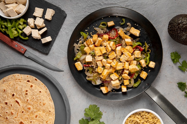 A close-up shot of a pan with tofu scramble with black beans and sliced avocado, garnished with fresh cilantro, showcasing the texture and vibrant colors of the dish. Steam is rising from the pan, indicating it's freshly made.