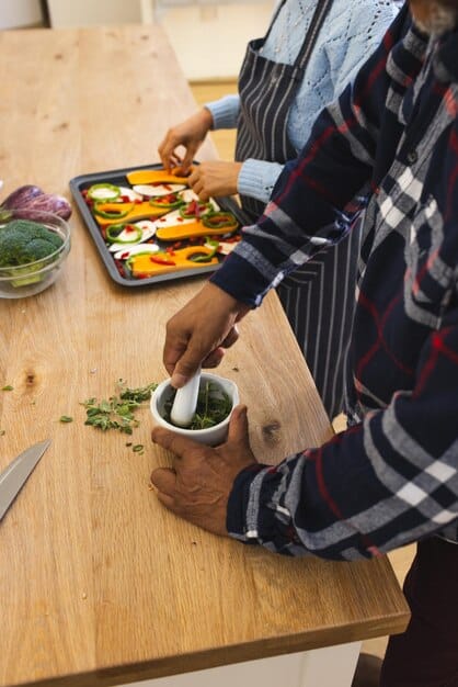 A person preparing curry in a kitchen, chopping fresh vegetables and adding spices to a pan. The kitchen is well-lit and modern, with various cooking utensils and ingredients visible.