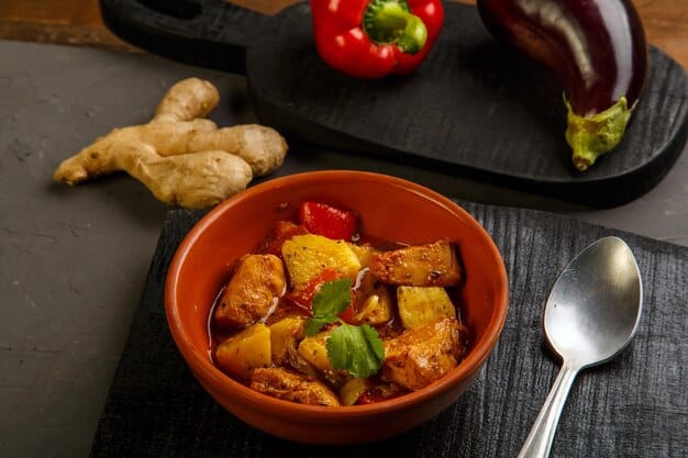 A close-up of a bowl of ginger chicken curry with vegetables, showcasing the variety of colorful vegetables and tender pieces of chicken. A spoon is dipping into the curry, highlighting the creamy texture.