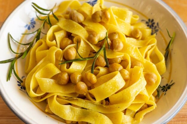 Elevated view of Mediterranean Chickpea Pasta, showcasing the texture of the pasta, the golden chickpeas, and the vibrant colors of chopped tomatoes and spinach. A drizzle of olive oil adds a glossy finish.