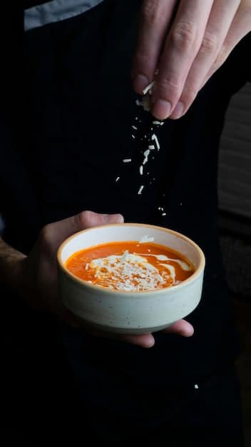 A vibrant orange soup being poured into a bowl. The soup is garnished with a swirl of coconut milk and a sprinkle of chopped cilantro.