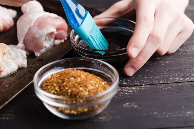 A close-up shot of a hand marinating chicken pieces in a glass bowl. The marinade is vibrant orange, indicating the presence of citrus and spices like paprika. The background shows a clean kitchen counter with various marinade ingredients.