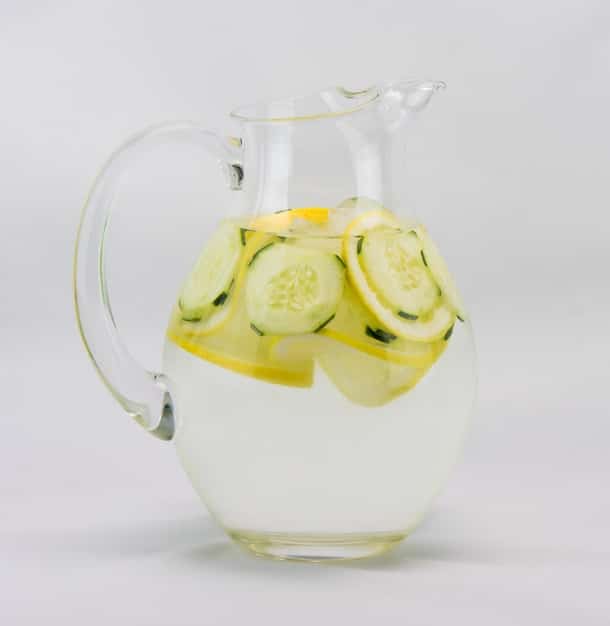 A close-up shot of a glass pitcher filled with cucumber and lemon detox water. Slices of cucumber and lemon are visible, along with a few sprigs of fresh mint. Condensation on the pitcher gives a sense of coolness and refreshment.